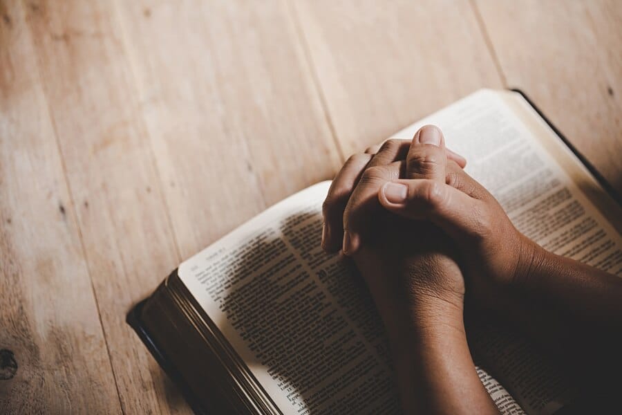 Mulher de mão entrelaçadas segurando a Biblia, expressando um momento de oração, reflexão e intimidade com Deus.
