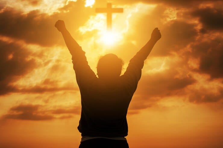 Uma pessoa de braços erguidos em direção ao céu, com um fundo dourado de pôr do sol e uma cruz iluminada ao fundo, simbolizando fé, entrega e conexão com Deus.