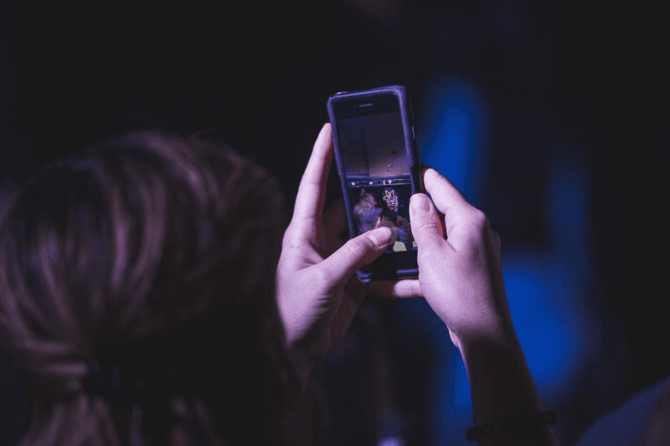 Mãos segurando smartphone em ambiente escuro com iluminação azul, capturando momentos para compartilhar em reels. A pessoa fotografa uma cena dinâmica, perfeita para criar conteúdo envolvente para redes sociais.